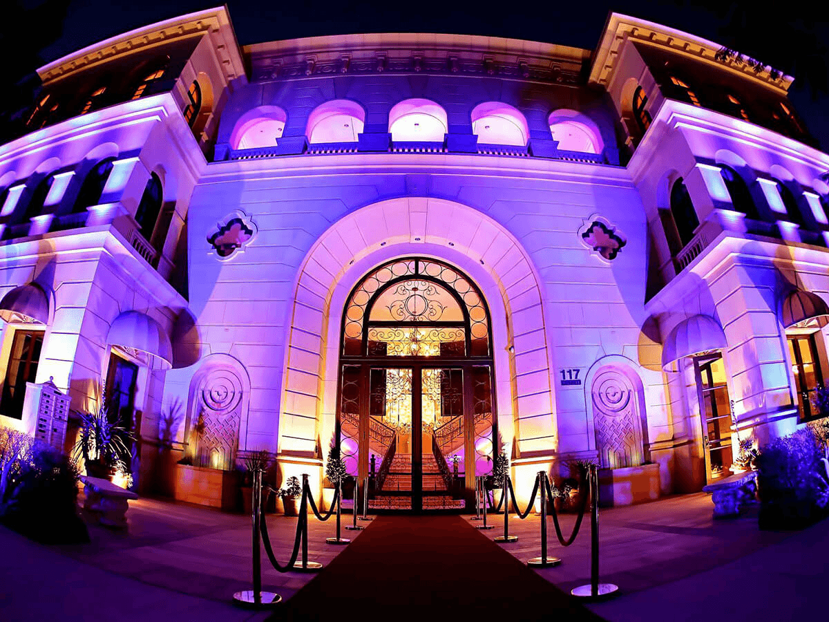 Elegant building entrance illuminated in purple, featuring a grand doorway, red carpet, and stylish decor.