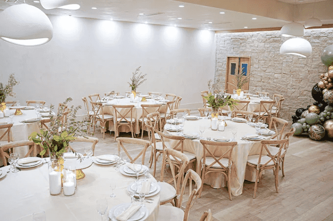 Elegant event space with round tables, neutral decor, greenery centerpieces, and warm lighting for gatherings.