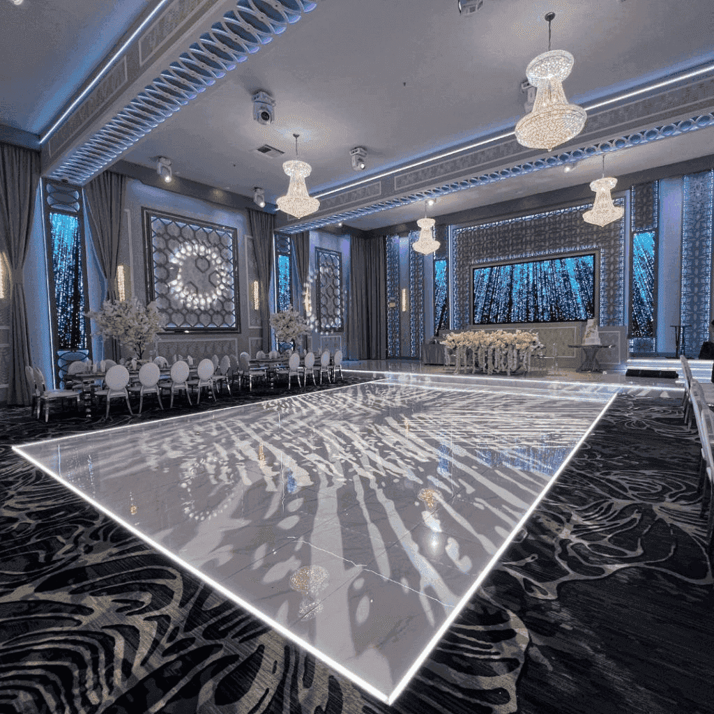 Elegant banquet hall featuring a illuminated dance floor, chandeliers, and stylish decor in soft blue and white tones.