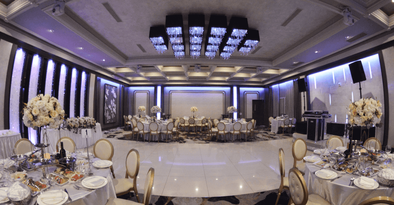 Elegant banquet hall with round tables, gold accents, floral centerpieces, and soft blue lighting, perfect for celebrations.