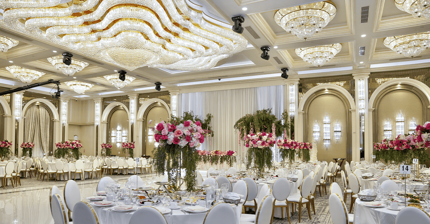 Elegant banquet hall with crystal chandeliers, pink floral centerpieces, and round dining tables set for a celebration.