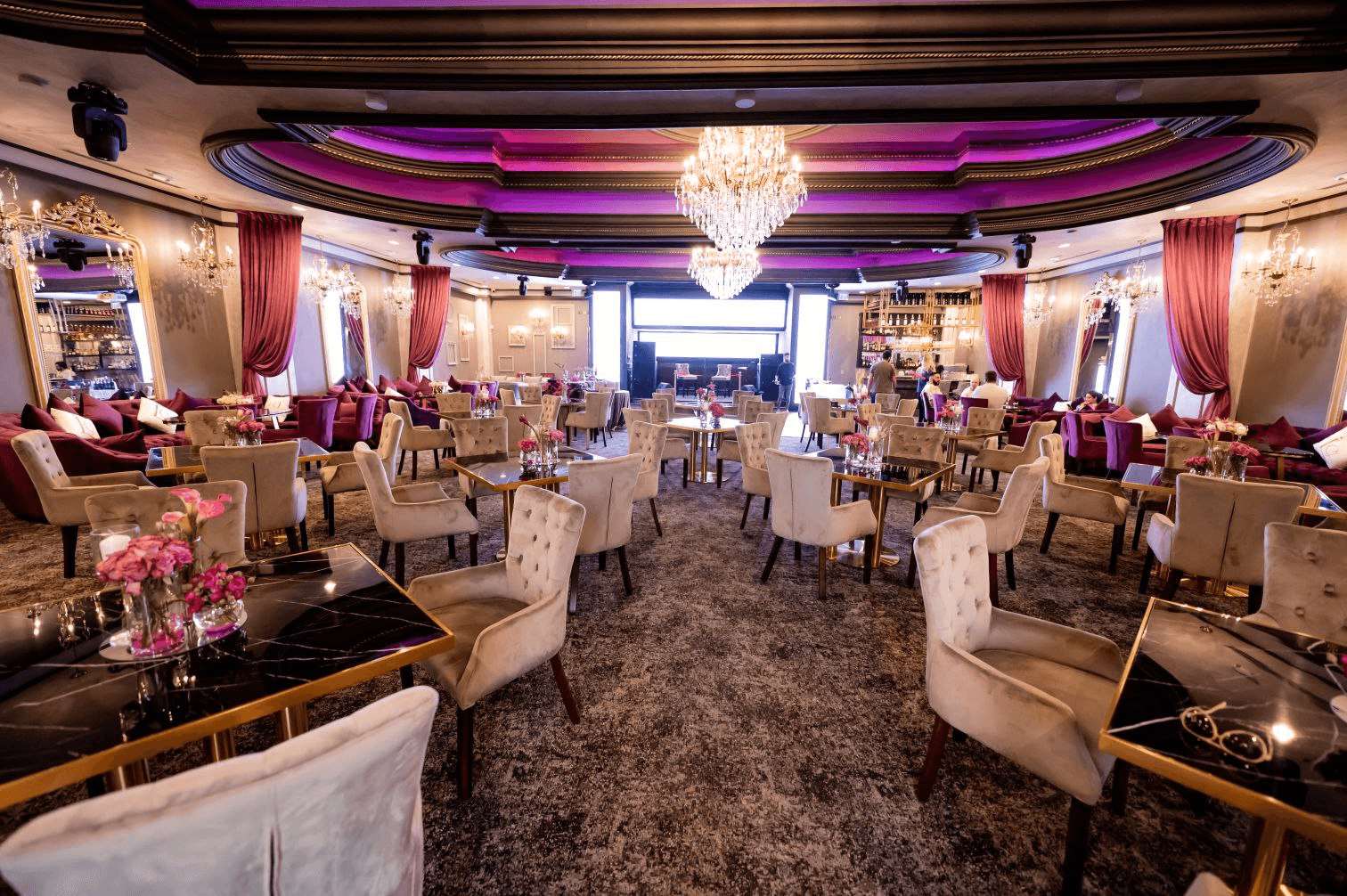 Elegant lounge with plush seating, gold accents, pink decor, and chandeliers, set for an upscale event or gathering.