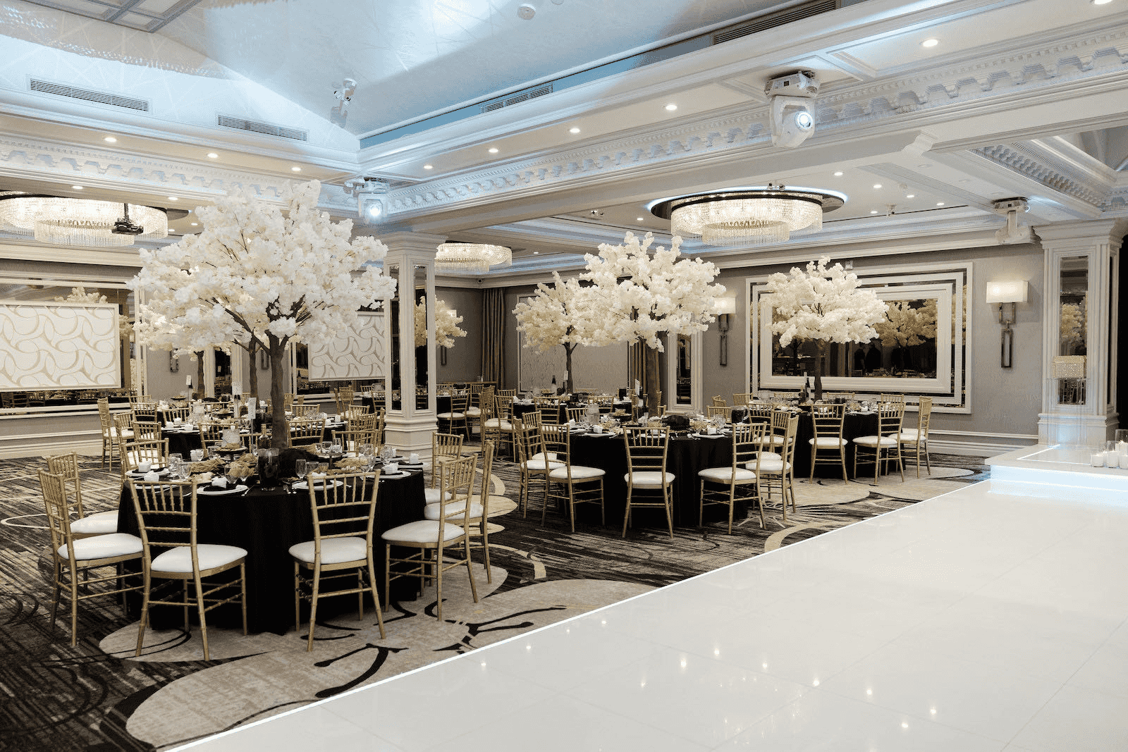 Elegant banquet hall with black tablecloths, gold chairs, floral decor, and bright chandeliers for formal events.