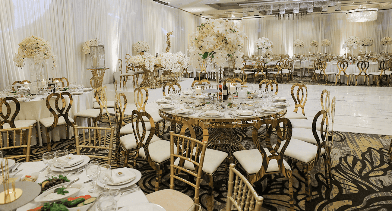 Elegant banquet hall with round gold tables, white floral centerpieces, and beautifully set dining decor.