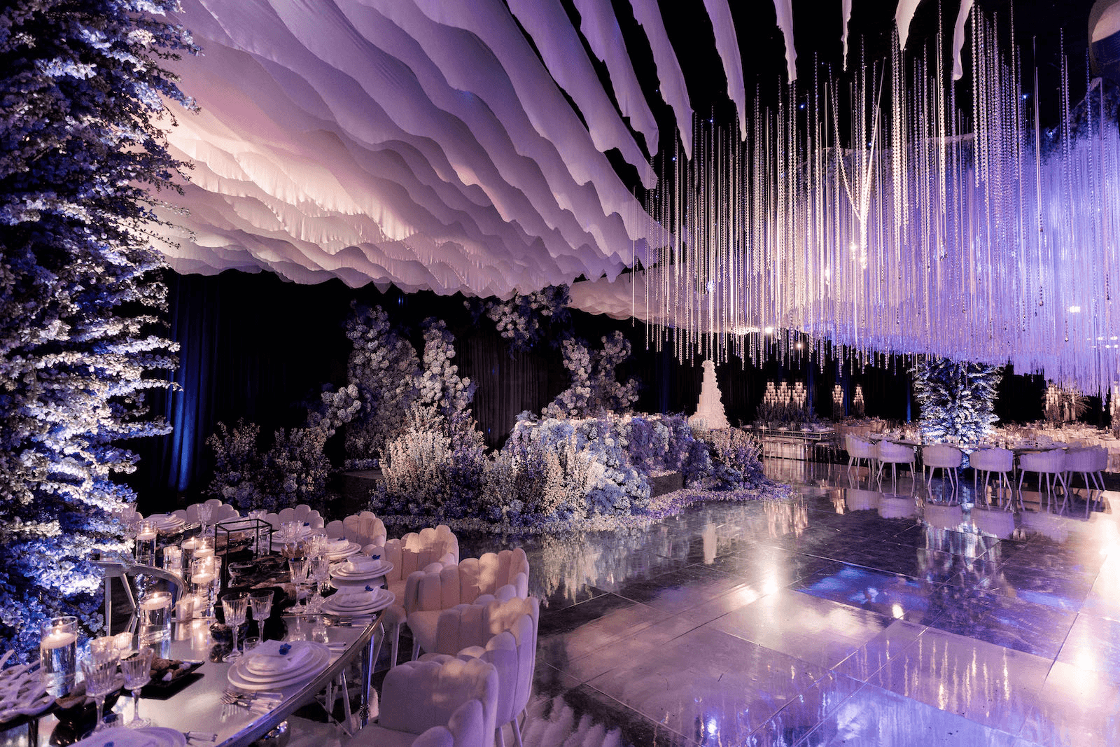Elegant banquet hall adorned in purple hues, featuring floral decorations, crystal chandeliers, and reflective tables.